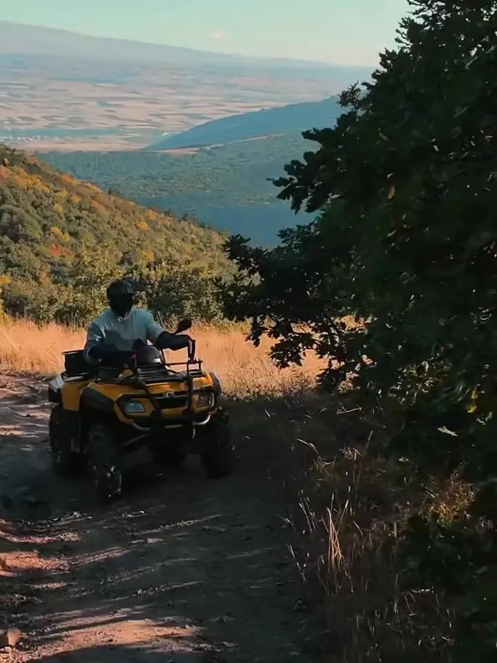 Yellow ATV on a trail overlooking a mountain valley