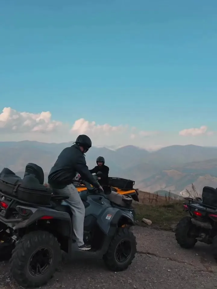 Riders by their ATVs on a mountain road with views of the ridges